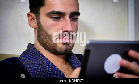 Junger Mann auf der Couch lesen mit Tablet-PC Stockfoto