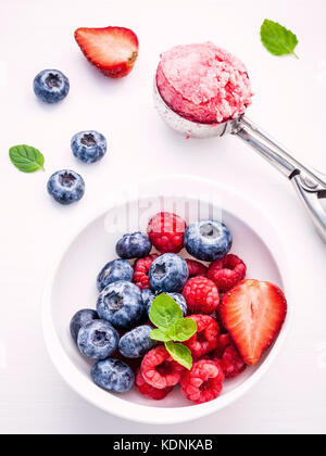 Nahaufnahme Eis mixed berry Früchte Himbeere, Heidelbeere, Erdbeere und Pfefferminze Blätter setup in Weiß Schüssel auf weißem Holz- Hintergrund. Sommer ein Stockfoto