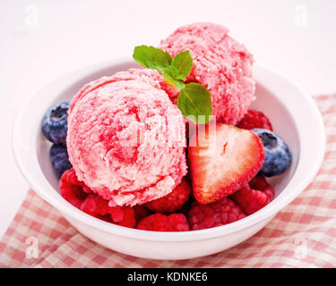 Nahaufnahme Eis mixed berry Früchte Himbeere, Heidelbeere, Erdbeere und Pfefferminze Blätter setup in Weiß Schüssel auf weißem Holz- Hintergrund. Sommer ein Stockfoto