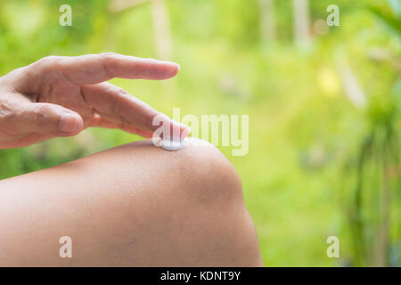 Hand der Frau gelten Lotion auf die Haut der Knie auf Natur Hintergrund. Stockfoto