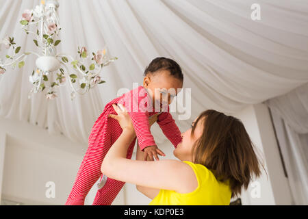 Glückliche Familie. Mutter wirft durcheinander Rennen Baby, zu Hause spielen Stockfoto