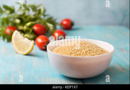 Couscous und frisches Gemüse: Tomaten, Zitrone, Petersilie auf einem blauen Hintergrund. Stockfoto