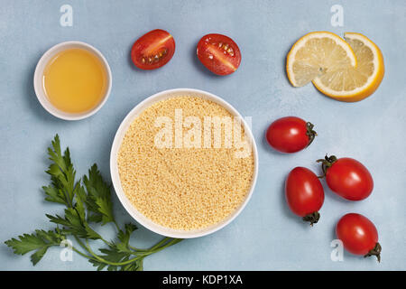 Couscous und frisches Gemüse: Tomaten, Paprika, Zitronensaft, Petersilie, Olivenöl auf einem blauen Hintergrund. Ansicht von oben Stockfoto