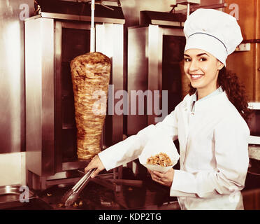 Professionelle fröhliche weibliche Kochen mit gegrilltem Fleisch am Spieß für Kebab Stockfoto