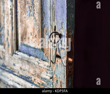 Eine Nahaufnahme der alten schäbigen Holztür mit Nieten und eine Klinke. Die Farbe abgeblättert und es gab Risse in seinen Platz. Stockfoto