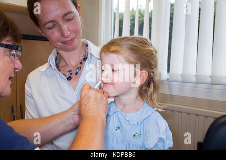 3 Jahre altes Kind, mit ihrer Mama/Mutter, erhält Dosis der Fluenz Grippeimpfstoff Nasenspray Immunisierung von NHS Praxiskrankenschwester UK. (90) Stockfoto