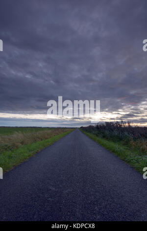 Eine Straße oder Gasse in Lincolnshire auf dem Venn in Flussauen entfernt verjüngt in die Ferne unter einem bewölkten bedrohlich grauen Himmel. Stockfoto