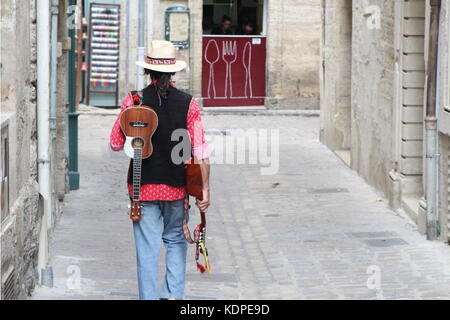 Musiker mit Strohfedorahut, Mandoline und Ukelele, die eine Kopfsteinpflasterstraße hinunter zu einem kleinen Café gehen Stockfoto
