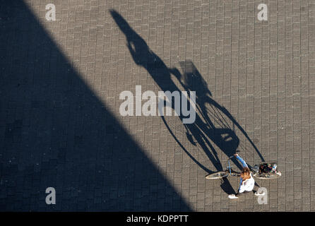Eine Frau, ein Fahrrad in die Sonne wirft einen langen Schatten auf die Hafencity in Hamburg, Deutschland, 15. Oktober 2017. Foto: Daniel bockwoldt/dpa Stockfoto