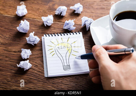 Hohe Betrachtungswinkel und der Person, die die Glühlampe der Notepad in der Nähe von zerknittertes Papier auf Holz Schreibtisch Stockfoto