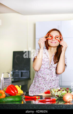 Frau in Schürze für ihre Augen mit Pfeffer und lächelnd in die Küche Stockfoto