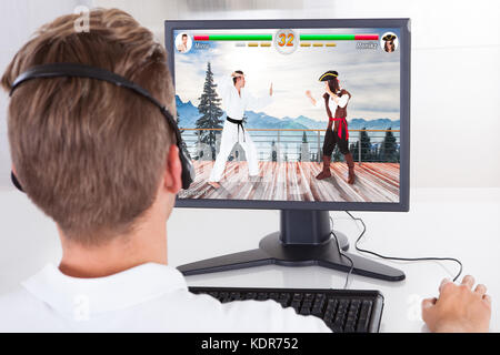Ansicht der Rückseite des Mann spielt Kampfspiel mit Hilfe der Kopfhörer auf dem Computer Desktop Stockfoto