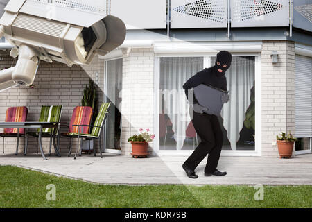 Sicherheit Kamera erfassen Dieb tragen Balaclava mit Laptop außerhalb des Hauses Stockfoto