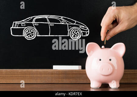 Person Hand einfügen Münze in Sparschwein mit Auto Bild auf der Tafel im Hintergrund Stockfoto