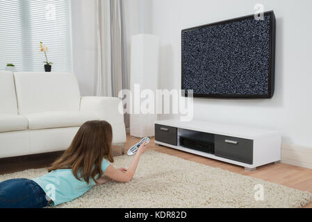 Mädchen Mit Fernbedienung Liegt Auf Dem Teppich Vor Dem Fernseher Ohne Signal Stockfoto