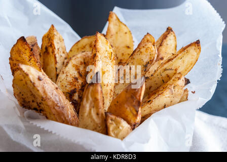 Gebackene Kartoffeln mit Gewürzen und Kräutern aus weißem Papier serviert - bereit zu essen Stockfoto