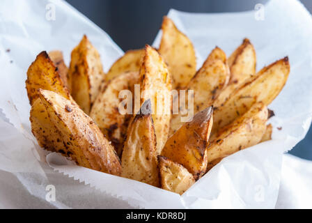 Gebackene Kartoffeln mit Gewürzen und Kräutern aus weißem Papier serviert - bereit zu essen Stockfoto