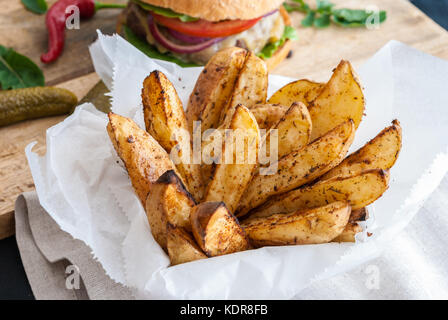 Gebackene Kartoffeln mit Gewürzen und Kräutern aus weißem Papier serviert - bereit zu essen Stockfoto