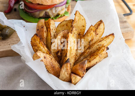 Gebackene Kartoffeln mit Gewürzen und Kräutern aus weißem Papier serviert - bereit zu essen Stockfoto