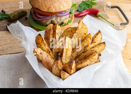 Gebackene Kartoffeln mit Gewürzen und Kräutern aus weißem Papier serviert - bereit zu essen Stockfoto