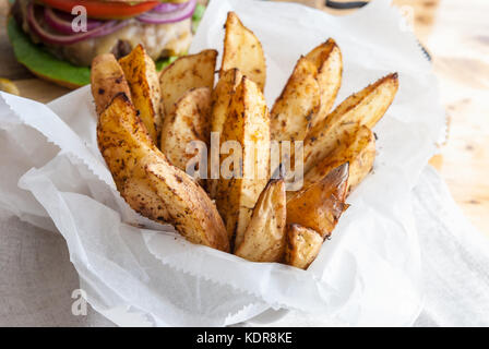 Gebackene Kartoffeln mit Gewürzen und Kräutern aus weißem Papier serviert - bereit zu essen Stockfoto