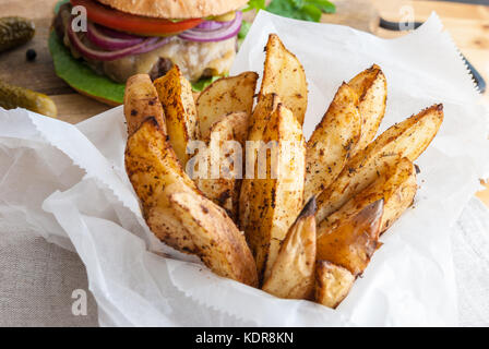 Gebackene Kartoffeln mit Gewürzen und Kräutern aus weißem Papier serviert - bereit zu essen Stockfoto