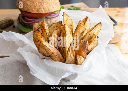 Gebackene Kartoffeln mit Gewürzen und Kräutern aus weißem Papier serviert - bereit zu essen Stockfoto