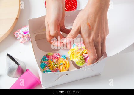 Nahaufnahme eines Konditor Frau Umhüllung in einem weißen Karton eine capcake mit Beeren, mit Sahne und Blumen auf einem weißen Tisch dekoriert Stockfoto