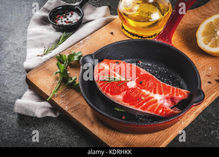 Rohe frische Lachs Fisch mit Zutaten zum Kochen - Olivenöl, Zitrone, Zwiebel, Petersilie, Rosmarin, auf der Pfanne, schwarzer Stein Tabelle, kopieren Raum Stockfoto