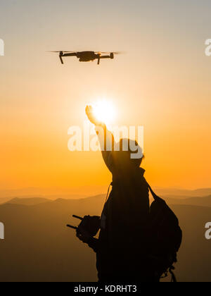 Silhouette des jungen Mannes, den Fang von drohne bei Sonnenuntergang für Fotos und Video - glückliche Menschen Spaß mit neuen technologischen Trends in Bergen Stockfoto