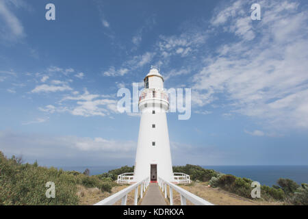 Tall classic Leuchtturm umgeben von Bush auf einer Klippe mit dem Meer im Hintergrund. strahlend blauen Himmel mit weichen Wolken Stockfoto