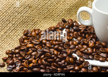 Nahaufnahme der Körner aus gerösteten Kaffee schwarz mit weißem Porzellan Schale auf Jutesäcken mit unscharfen Hintergrund und Platz für Text Stockfoto