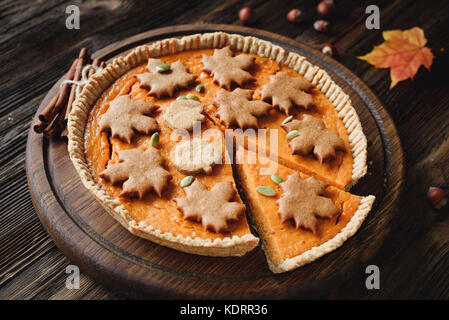 Hausgemachte Pumpkin Pie mit Lebkuchen zimt Cookies auf Holztisch mit einer Scheibe ausgeschnitten. Ganze kürbistorte eingerichtet Stockfoto