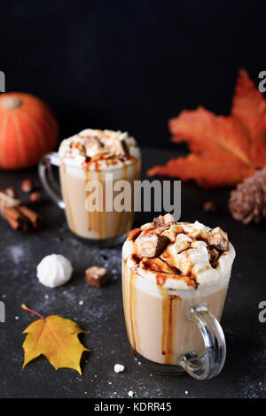 Pumpkin spice Latte mit Schlagsahne, Karamellsauce und Schokoriegel auf schwarzem Hintergrund. Vertikale, kopieren Platz für Text. Herbst Komfort Essen Stockfoto