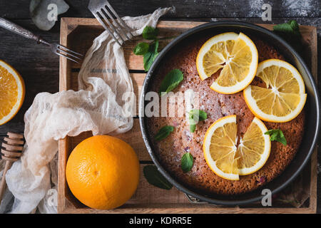 Orange Kuchen mit Orangenscheiben und minzeblatt auf Holz fach Top View eingerichtet. Essen still life Stockfoto