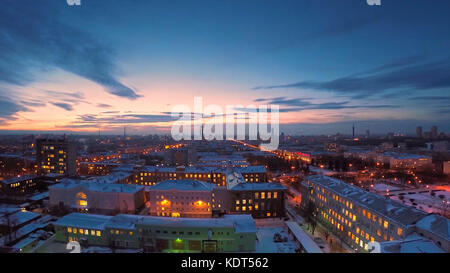 Abendliche Stadt im Winter Zeitraffer. Abendliche Stadt im Winter Blick vom Dach Zeitraffer. Panoramablick auf die Stadt und die Dächer unter dem Schnee, Zeitraffer. Straßenbeleuchtung bei Nacht Stockfoto