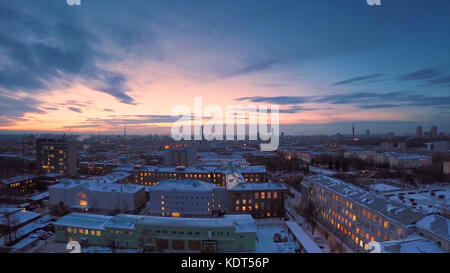 Abendliche Stadt im Winter Zeitraffer. Abendliche Stadt im Winter Blick vom Dach Zeitraffer. Panoramablick auf die Stadt und die Dächer unter dem Schnee, Zeitraffer. Straßenbeleuchtung bei Nacht Stockfoto