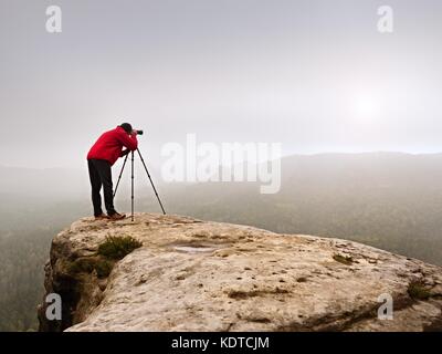 Photographr in den Sucher der DSLR-Kamera auf Stativ. Künstler fotografieren Berg und trübe Landschaft. Man prüfen Bild auf Stockfoto