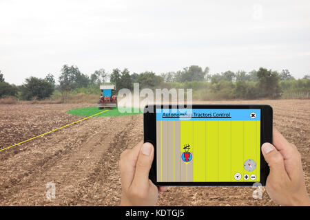 Smart Landwirtschaft Konzept, Landwirt mit Tablet autonomen Traktor zu steuern, während die Erde im Feld, der Traktor mit Pflug beim Arbeiten und können Co Stockfoto