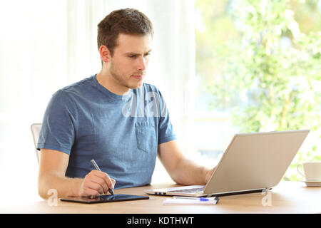 Ernster mann Zeichnung mit einem Stift und einem Laptop auf einen Desktop zu Hause Stockfoto