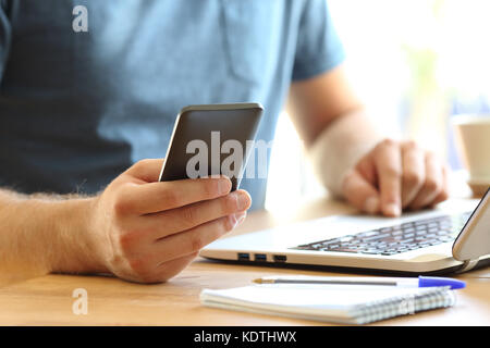 Nahaufnahme von einem Mann mit einem Smartphone und Laptop auf einem Desktop-PC zu Hause oder im Büro Stockfoto