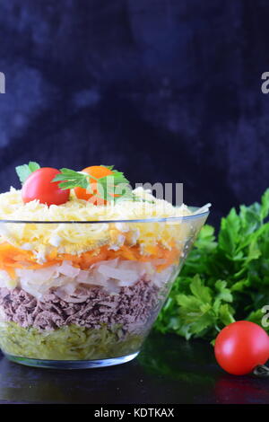 Salat mit Huhn Leber in Schichten mit Gurken, gekochte Karotten, Eier, Käse in eine Glasschüssel auf einem schwarzen Abstrakt Hintergrund. top anzeigen. Gesundes Essen conc Stockfoto