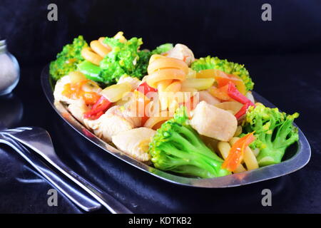 Gebratenes Hähnchenbrustfilet mit Gemüse und Nudeln in eine Wanne aus Metall auf einem schwarzen abstrakt hintergrund Rühren Stockfoto