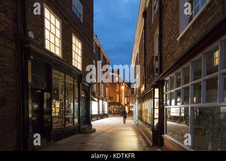 Abend Blick entlang Münster Tore im Zentrum von York, North Yorkshire, England, Grossbritannien - urig, schmalen Weg, gesäumt von Geschäften, einigen geschlossenen, einige bis lit. Stockfoto