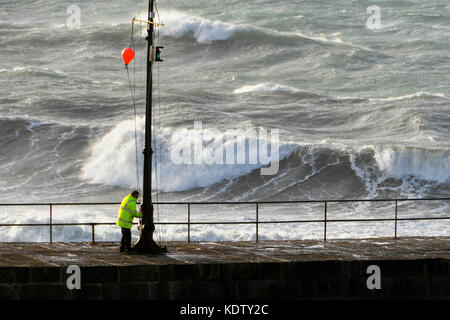 Camborne, Cornwall, England. 16 Okt, 2017. UK Wetter. Ein Hafen offizielle heben eine rote Warnmeldung Ball ein Pol auf der Hafenmauer als Gale force Winds aus ex Hurrikan Ophelia peitschen bis stürmischer See in der Küstenstadt Porthleven in Cornwall. Photo Credit: Graham Jagd-/Alamy leben Nachrichten Stockfoto