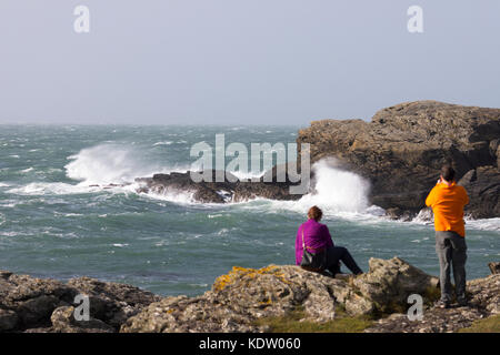 Anglesey, Wales. 16 Okt, 2017. UK Wetter. Wie prognostiziert mit Gelb und Gelb und die gefährlichere rote Warnungen, die durch die Met Office beginnt landfall Hurrikan Ophelia wird zu den meisten westlichen Teilen des Vereinigten Königreichs einschließlich Wales Sturm Wetter und Meer bringen Überspannungen wie dieses Paar entdeckt Fotografieren der Wellen gefährlich nah an das Meer Flanke an Treaddur Bay, Anglesey Stockfoto