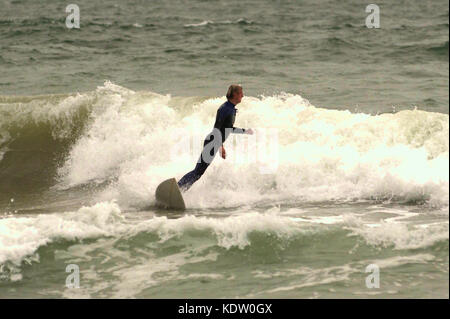 Surfer in einem Neoprenanzug im Winter auf einer Welle und am Rande des Sturms Ophellia in Boscombe, Bournemouth, Dorset, Großbritannien. Stockfoto