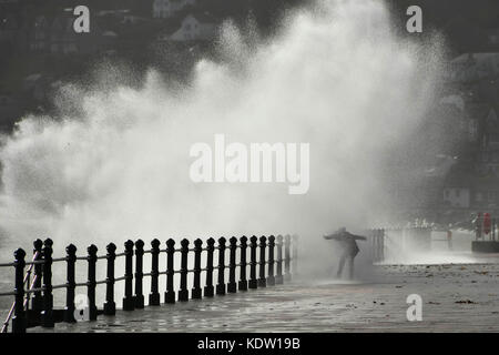 Penzance, Cornwall, UK. 16. Oktober 2017. UK Wetter. Ein Nervenkitzel sucht Frau erhält eine Tiefe, wie Sie vor einem plätschernden Wellen, die auf der Promenade von Penzance in Cornwall, der von Gale force Winds aus ex Hurrikan Ophelia gepeitscht wurde. Photo Credit: Graham Jagd-/Alamy leben Nachrichten Stockfoto