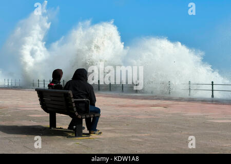 Penzance, Cornwall, UK. 16. Oktober 2017. UK Wetter. Zwei Menschen zusehen, wie Wellen splash als Hit der Promenade, der von Gale force Winds aus ex Hurrikan Ophelia von Penzance in Cornwall gepeitscht wurden. Photo Credit: Graham Jagd-/Alamy leben Nachrichten Stockfoto