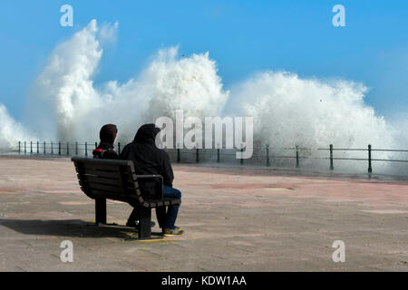 Penzance, Cornwall, UK. 16. Oktober 2017. UK Wetter. Zwei Menschen zusehen, wie Wellen splash als Hit der Promenade, der von Gale force Winds aus ex Hurrikan Ophelia von Penzance in Cornwall gepeitscht wurden. Photo Credit: Graham Jagd-/Alamy leben Nachrichten Stockfoto